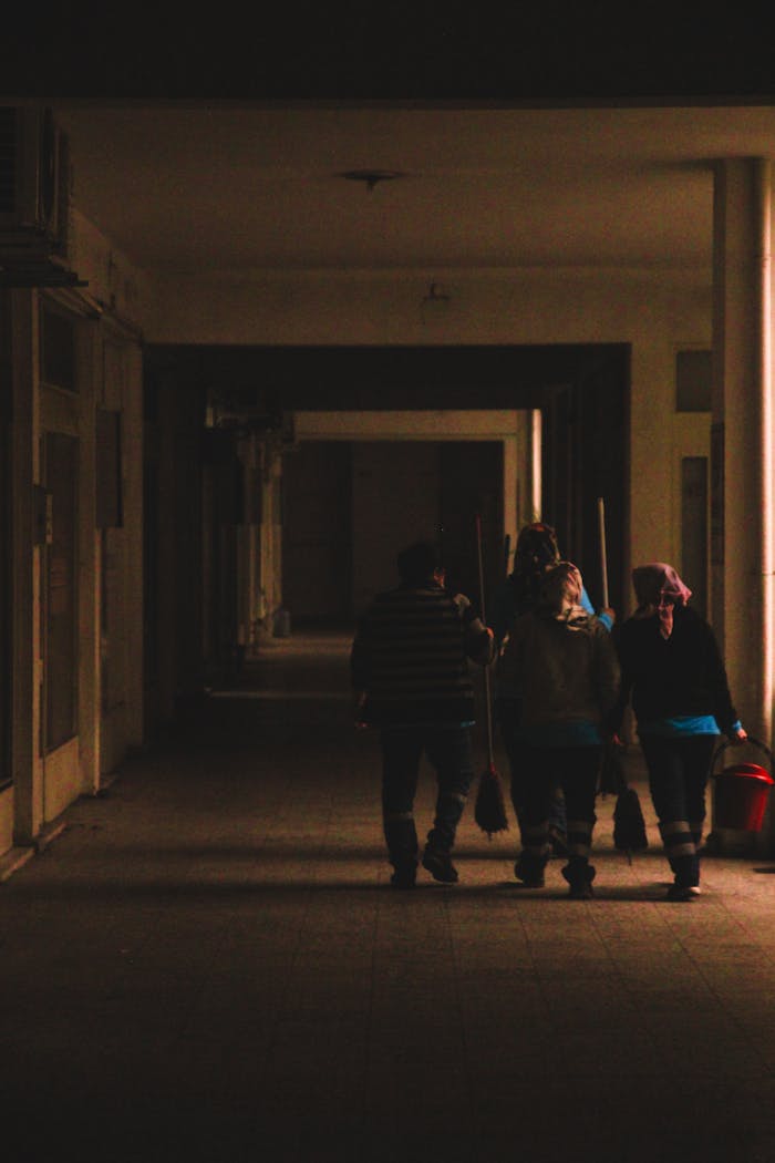 services-02 A group of adults walking together through a dimly lit indoor hallway, holding cleaning supplies.