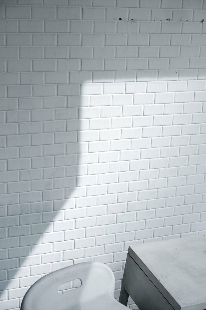 team-02 A minimalist white brick wall casting a shadow, paired with a modern chair and table.
