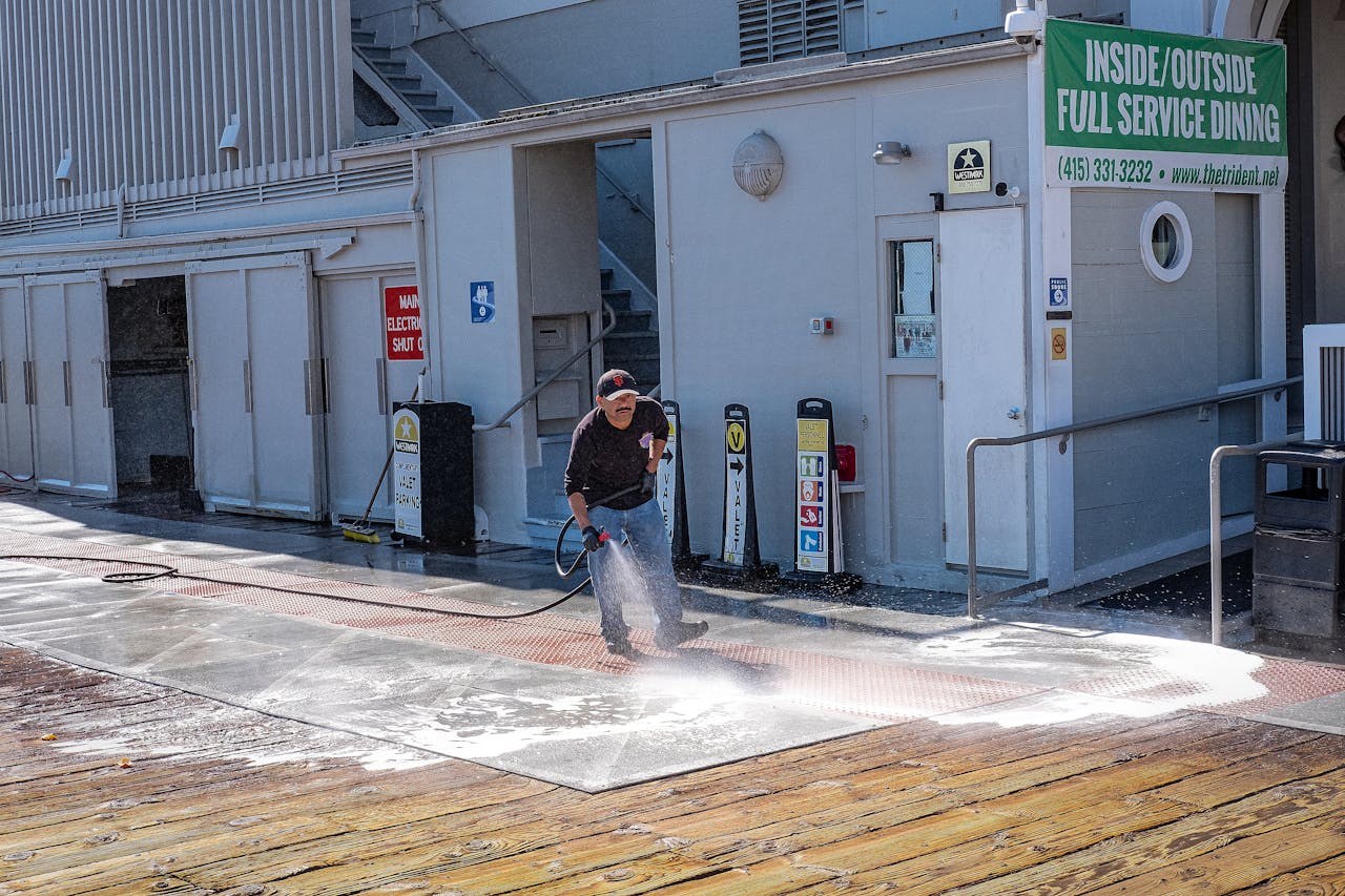 why-choose-us A worker uses a pressure washer to clean a sidewalk outside a dining facility.
