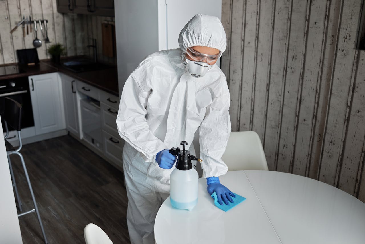 services-03 Person wearing PPE cleans a table indoors with sanitizer during pandemic.