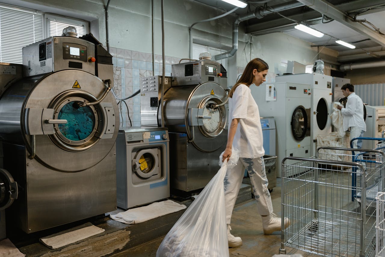 services-02 Busy industrial laundry with workers handling large washing machines.