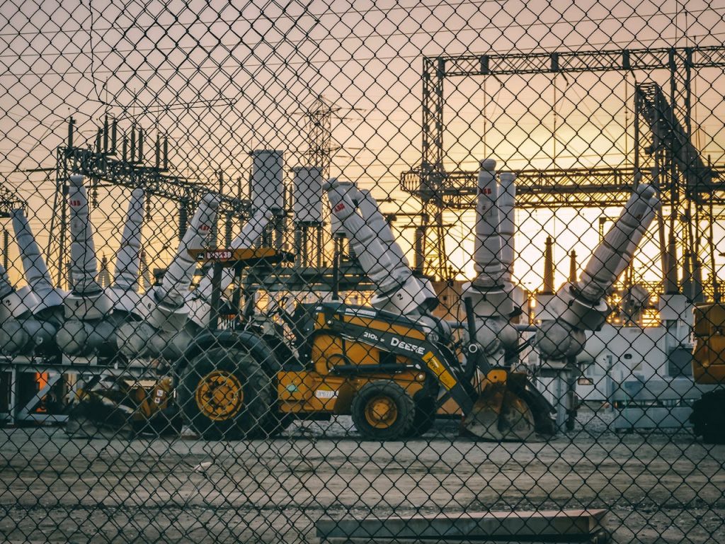 pexels-photo-9889054 An industrial power plant with heavy machinery and equipment behind a chain link fence during sunset, showcasing energy infrastructure.